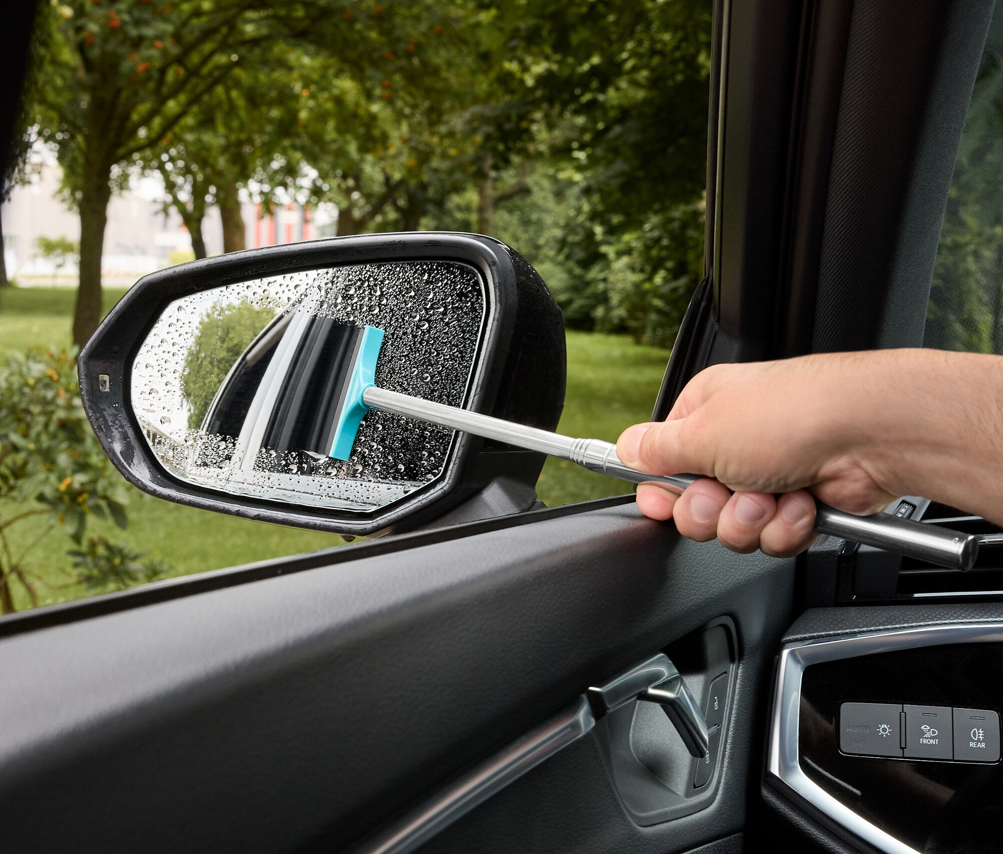 Muž stiera vodu z bočného zrkadla auta stierkou s modrou gumou.