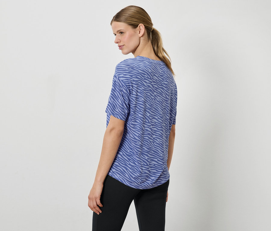 Žena v modrom tope so zvieracou potlačou a čiernych nohaviciach, pozerá cez rameno.