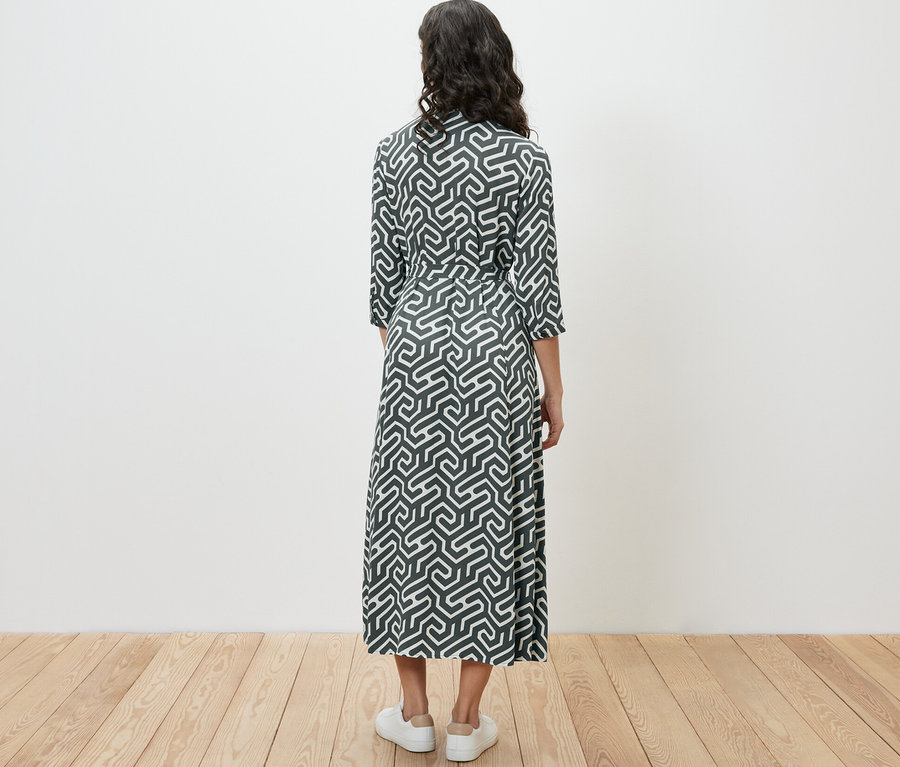 Žena stojí chrbtom a má na sebe košeľové šaty s potlačou.