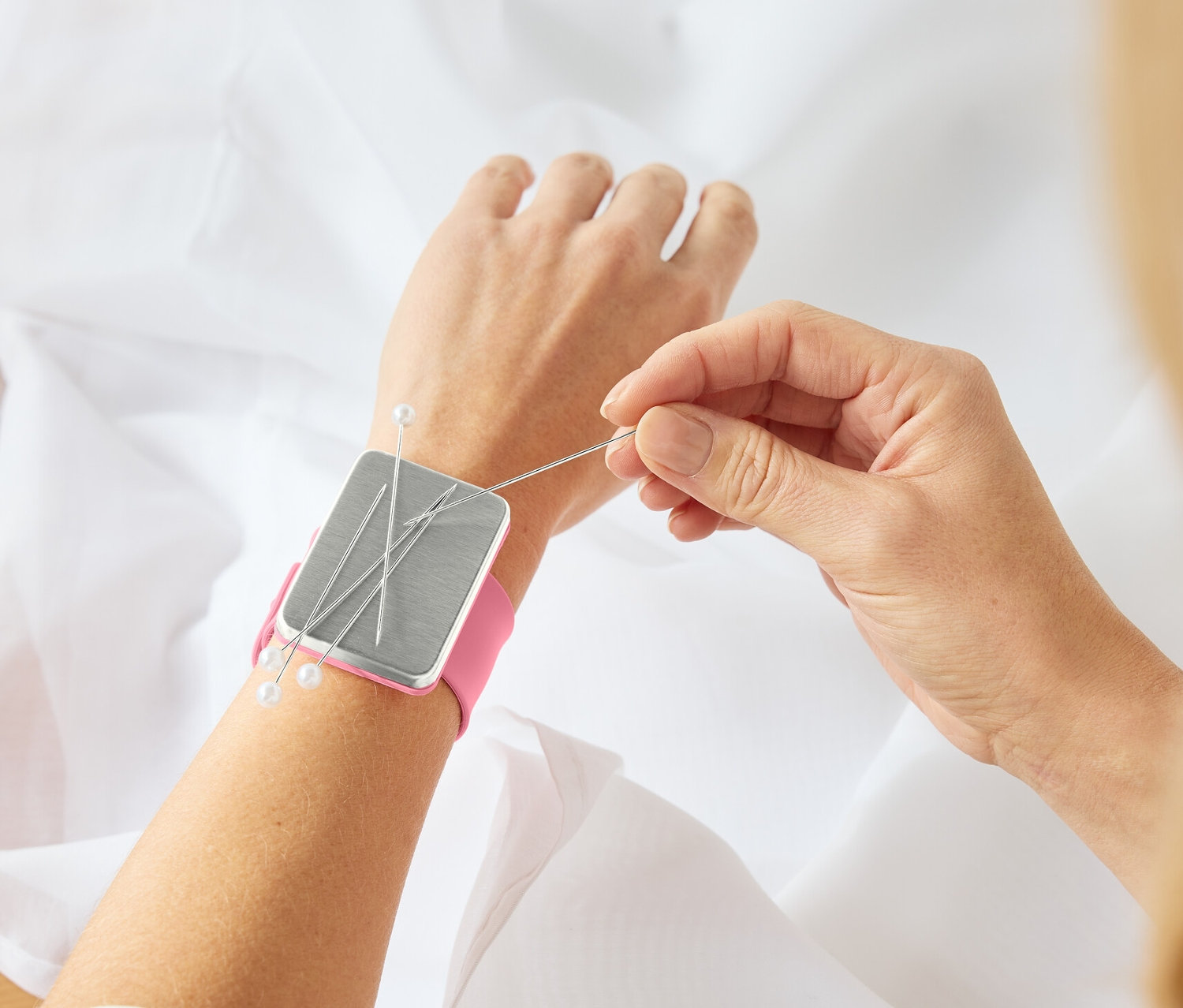 Žena šije látku s magnetickým držiakom ihiel Armnadelkissen na zápästí.