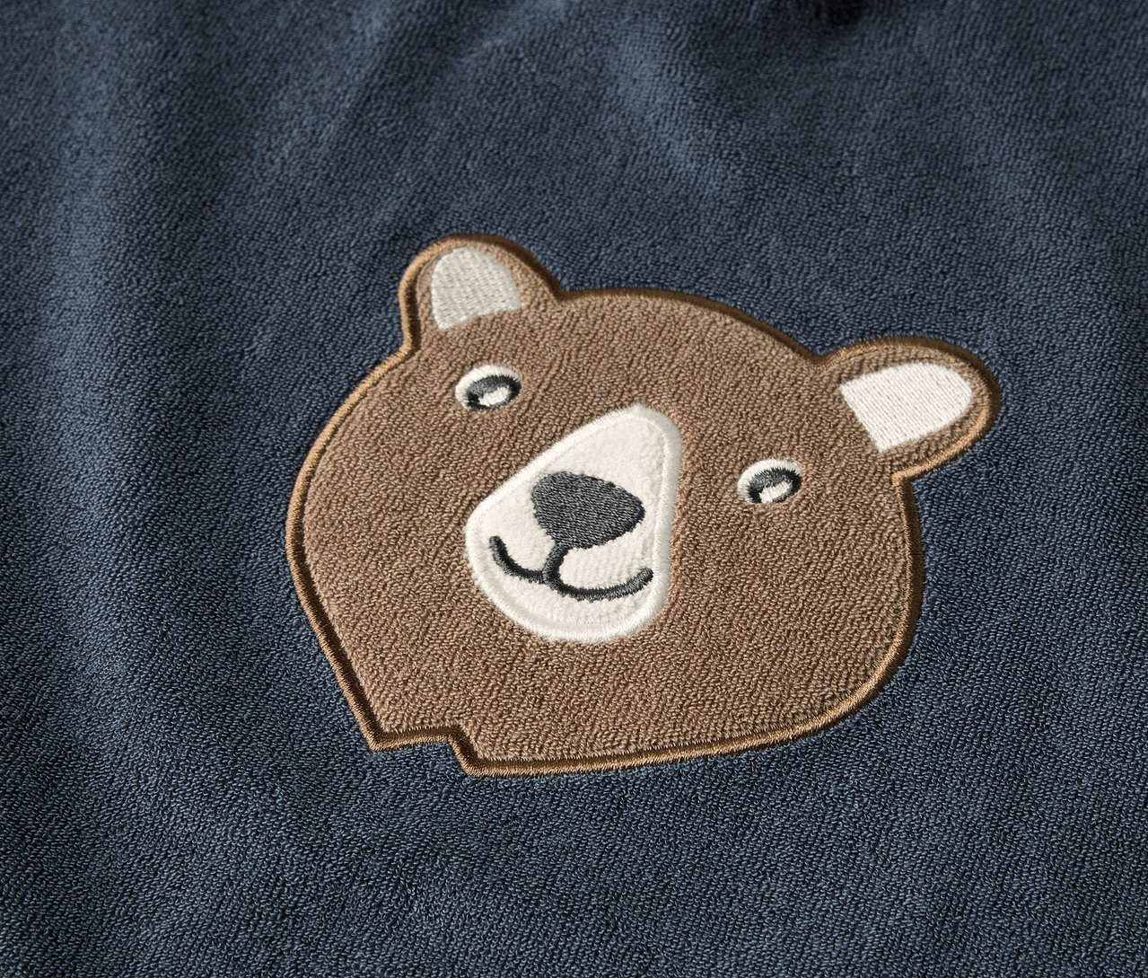 Detail detského froté ponča s hnedou nášivkou medvedej hlavy.