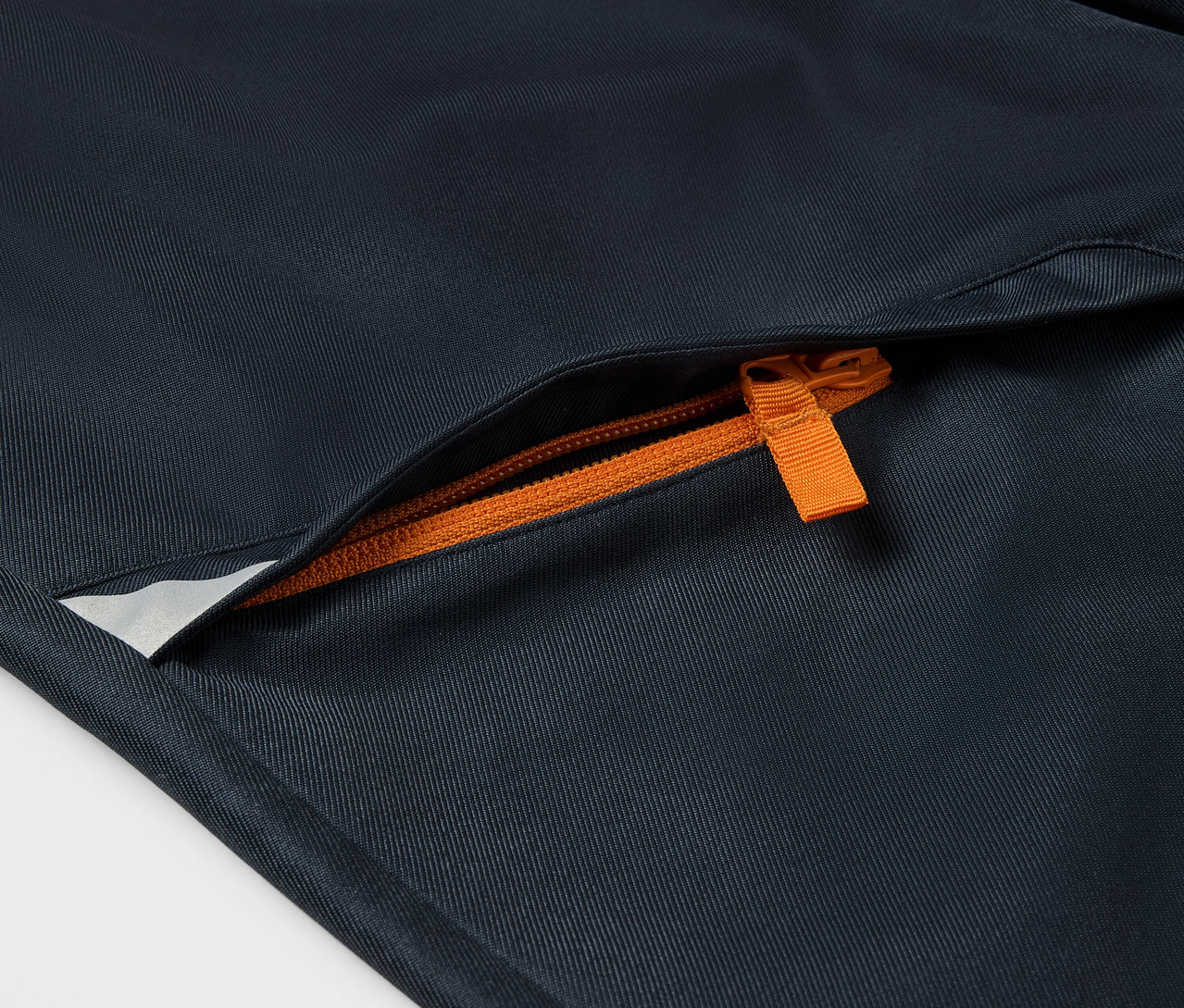 Detail detských softshellových nohavíc s oranžovým zipsom na vrecku.