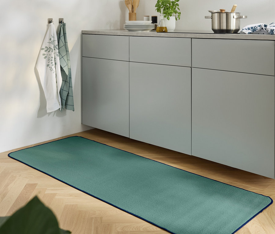 Zelený koberec leží na drevenej podlahe v kuchyni so sivou skrinkou.
