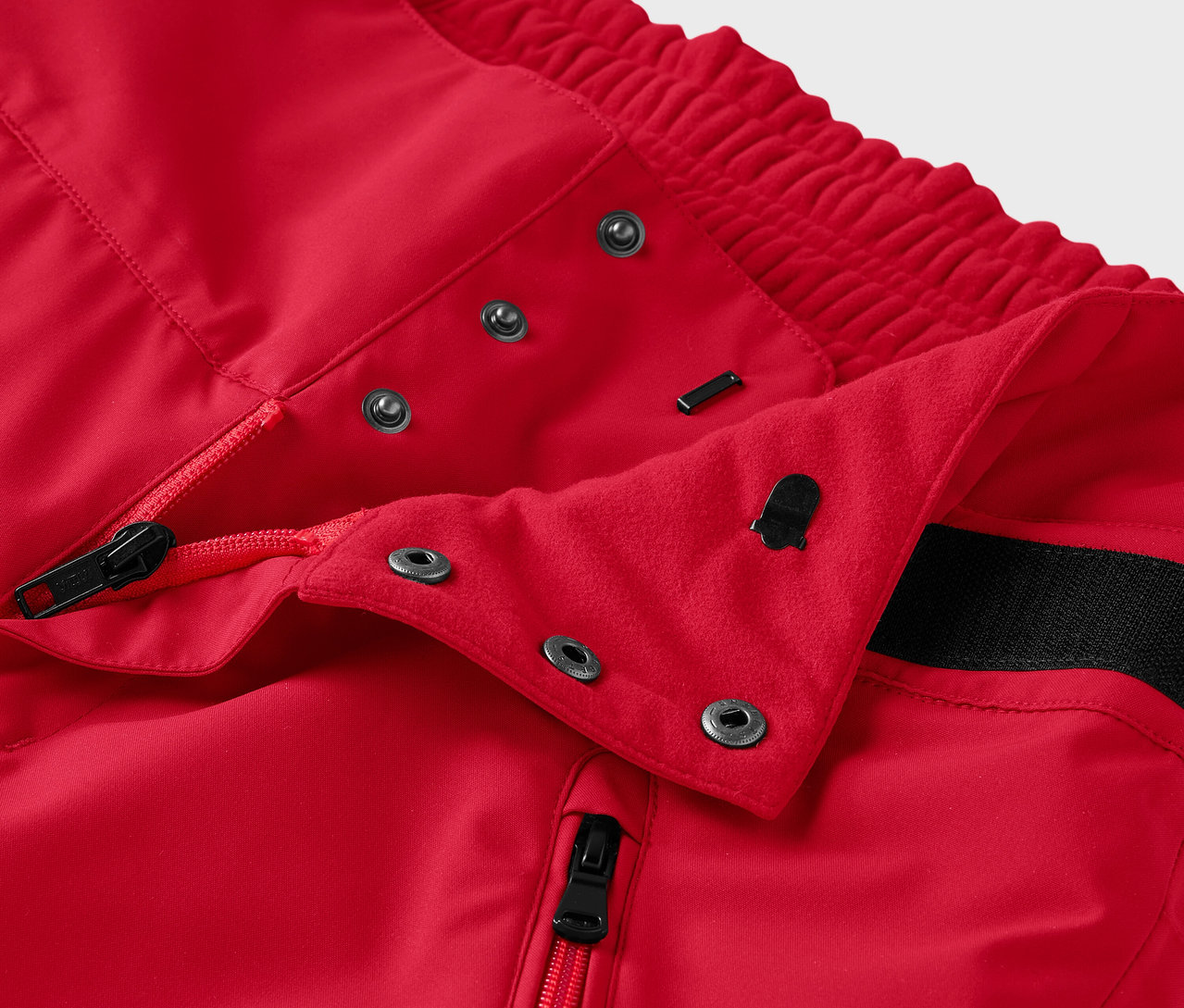 Detail červených nohavíc so zipsom a patentkami.