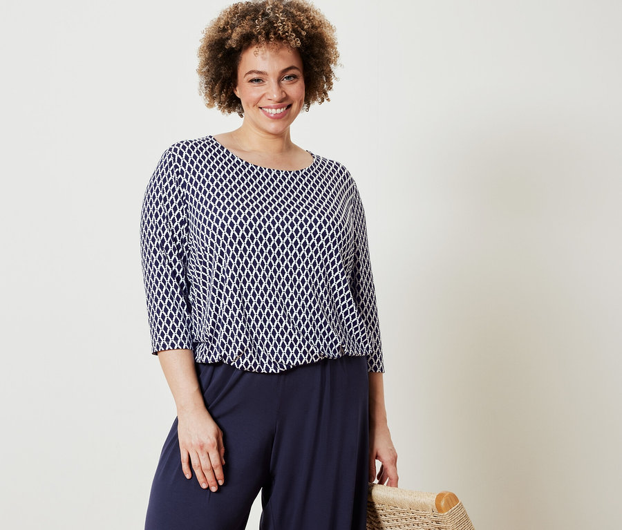 Žena pózuje v blúzkovom tričku s potlačou a tmavomodrých nohaviciach v štýle palazzo.