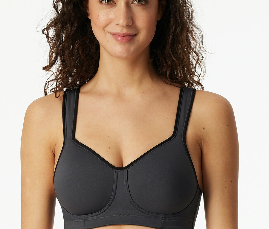 Usmievajúca sa žena má na sebe sivú športovú podprsenku.