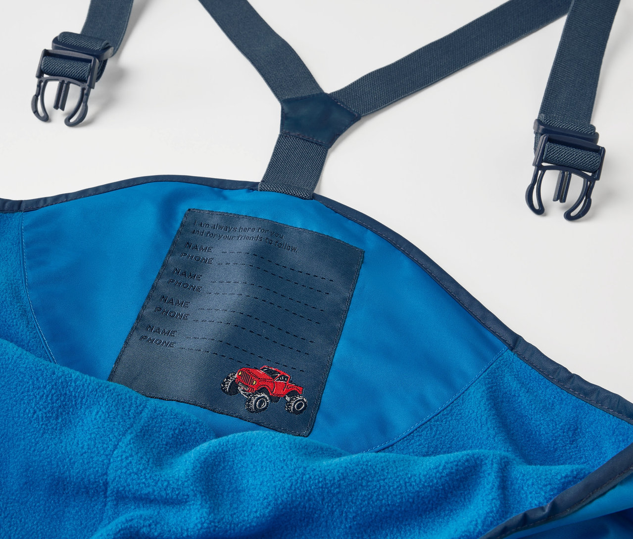 Detail modrých detských termo nohavíc do dažďa s náprsenkou a nášivkou červeného auta.