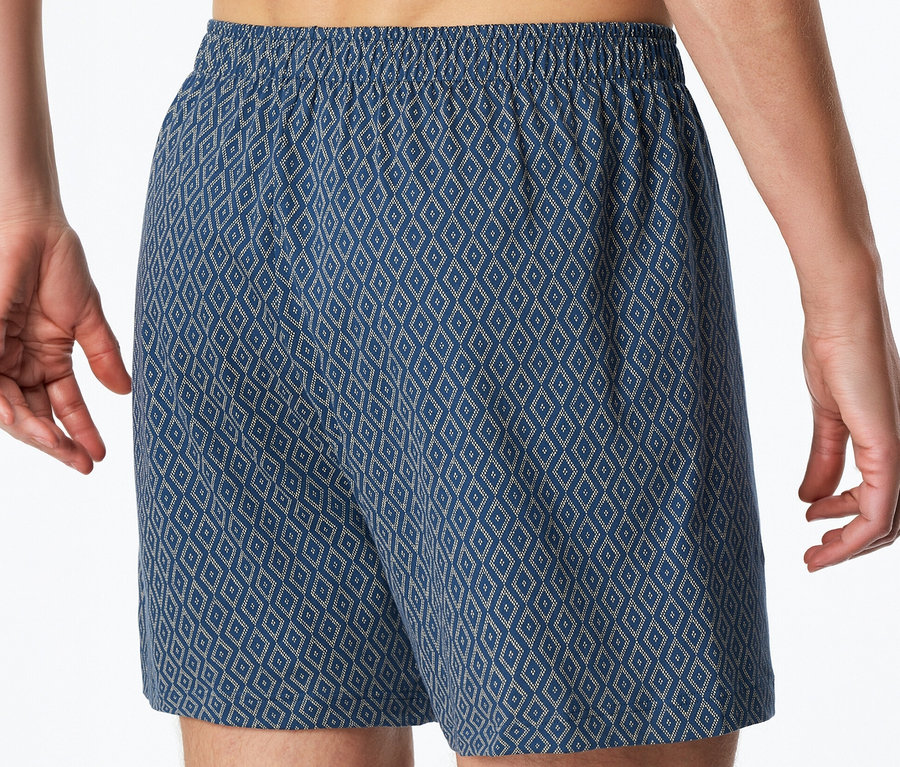 Muž má na sebe modré džersejové boxerky SCHIESSER s kosoštvorcovým vzorom a elastickým pásom.