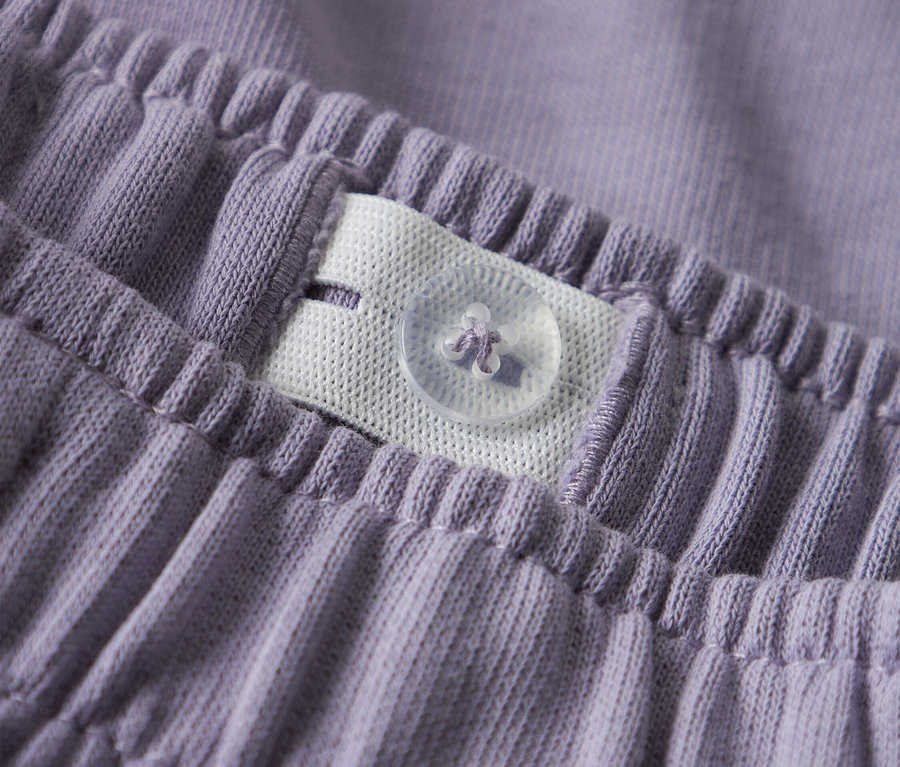 Detailný záber na pás fialových nohavíc s nastaviteľnou gumičkou a gombíkom.