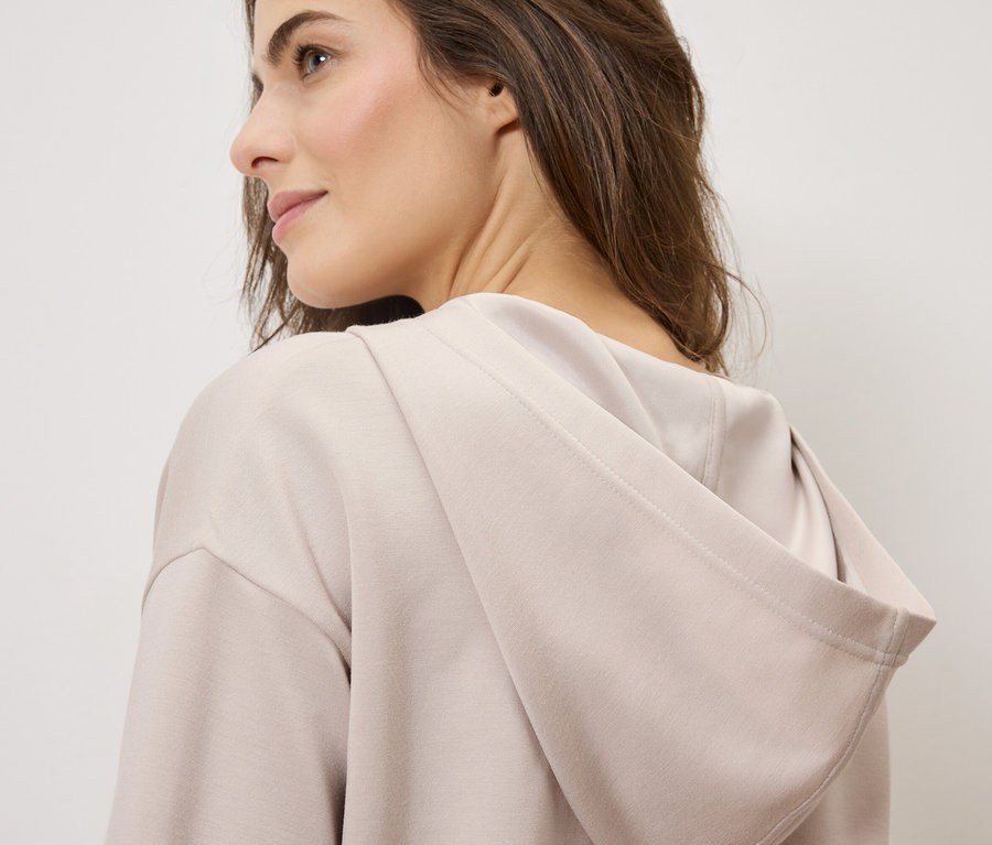 Žena má na sebe svetlohnedú mikinu s kapucňou.