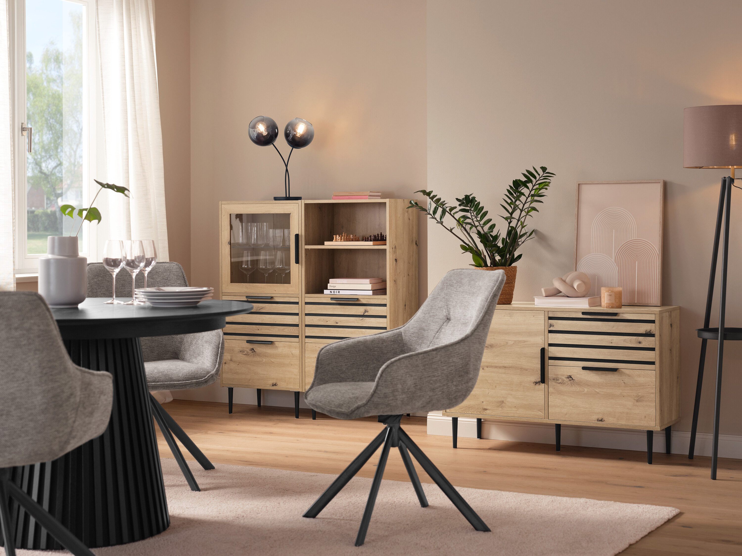 Jedáleň s okrúhlym stolom, sivými stoličkami, vitrínou »BAAKEN« s presklenými dverami, regálom »BAAKEN« so zásuvkami a príborníkom so zásuvkami.