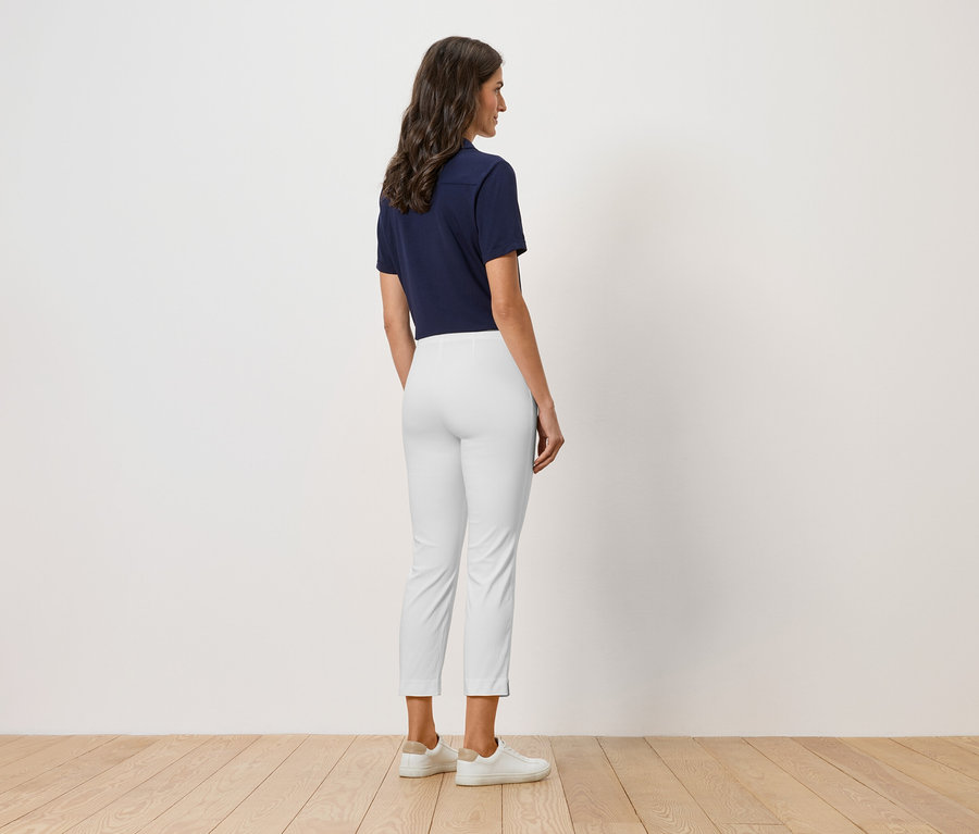 Žena stojí chrbtom k fotoaparátu, má na sebe tmavomodré polo tričko, biele nohavice a biele topánky.