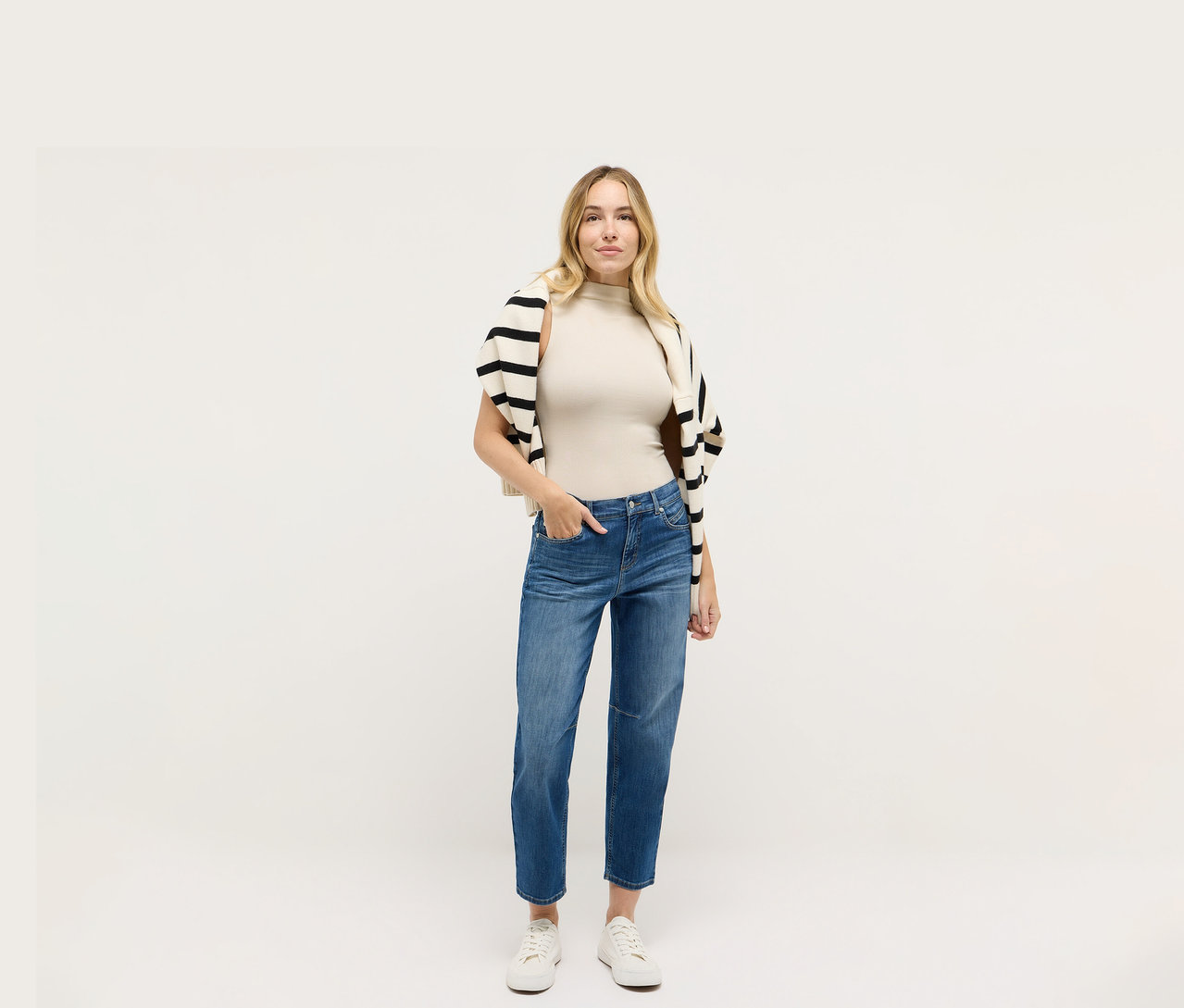 Žena v džínsoch Angels Denim »Evi«, béžovom tope a čierno-bielom pruhovanom svetri.