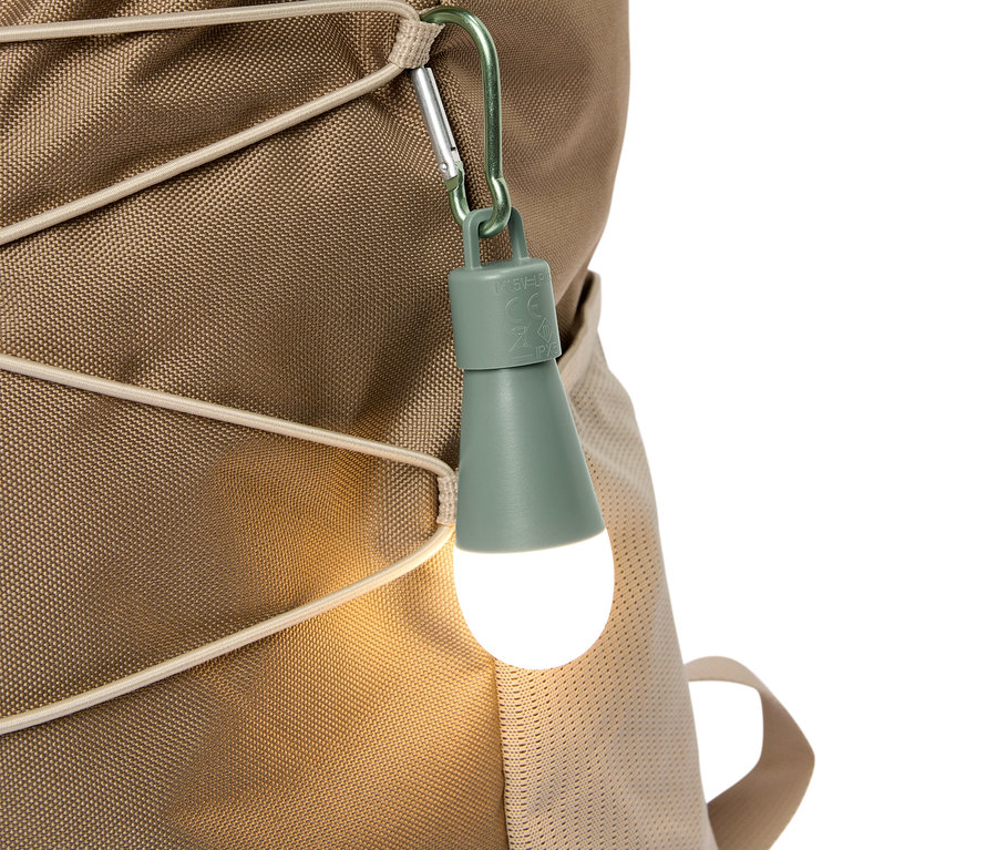 Detailný záber olivovo zeleného LED svetla pripevneného karabínou k béžovému ruksaku.