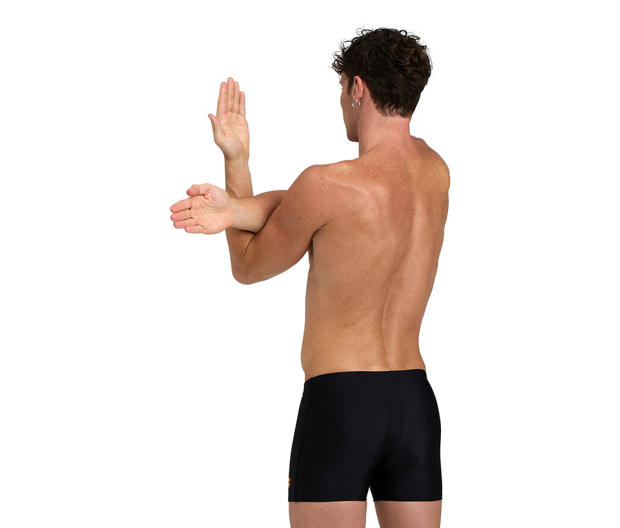 Muž si naťahuje ruky, má na sebe čierne plavky.