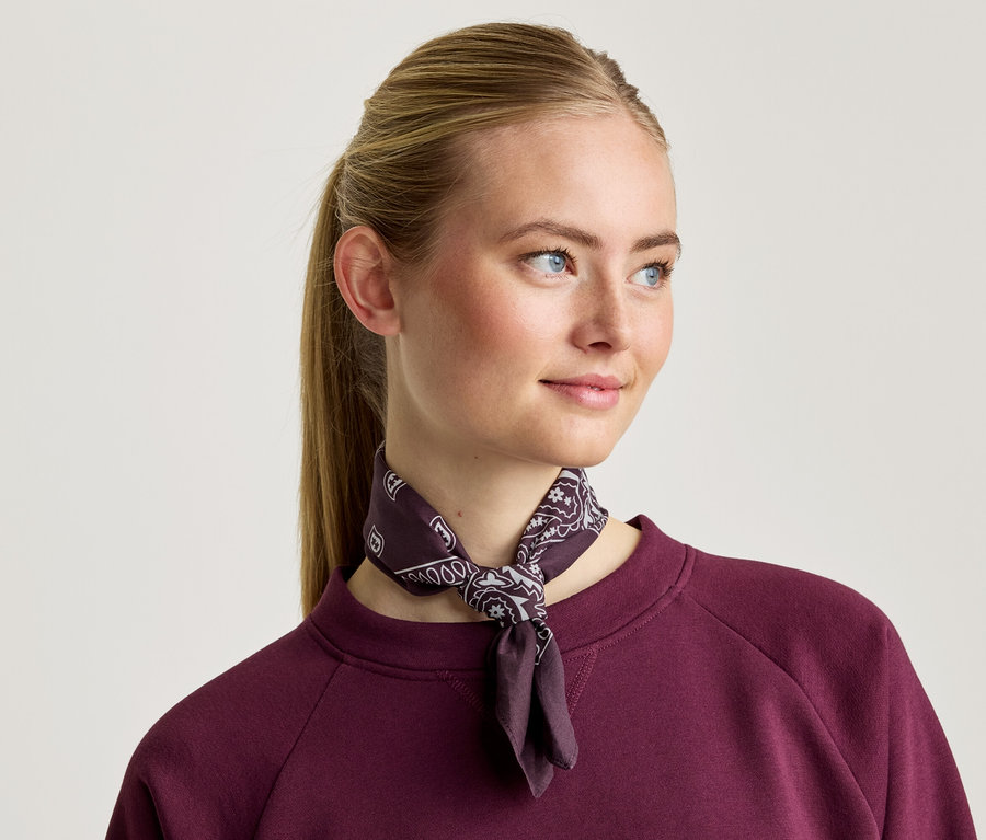 Žena s blond vlasmi má na sebe bordovú mikinu a vzorovanú šatku.
