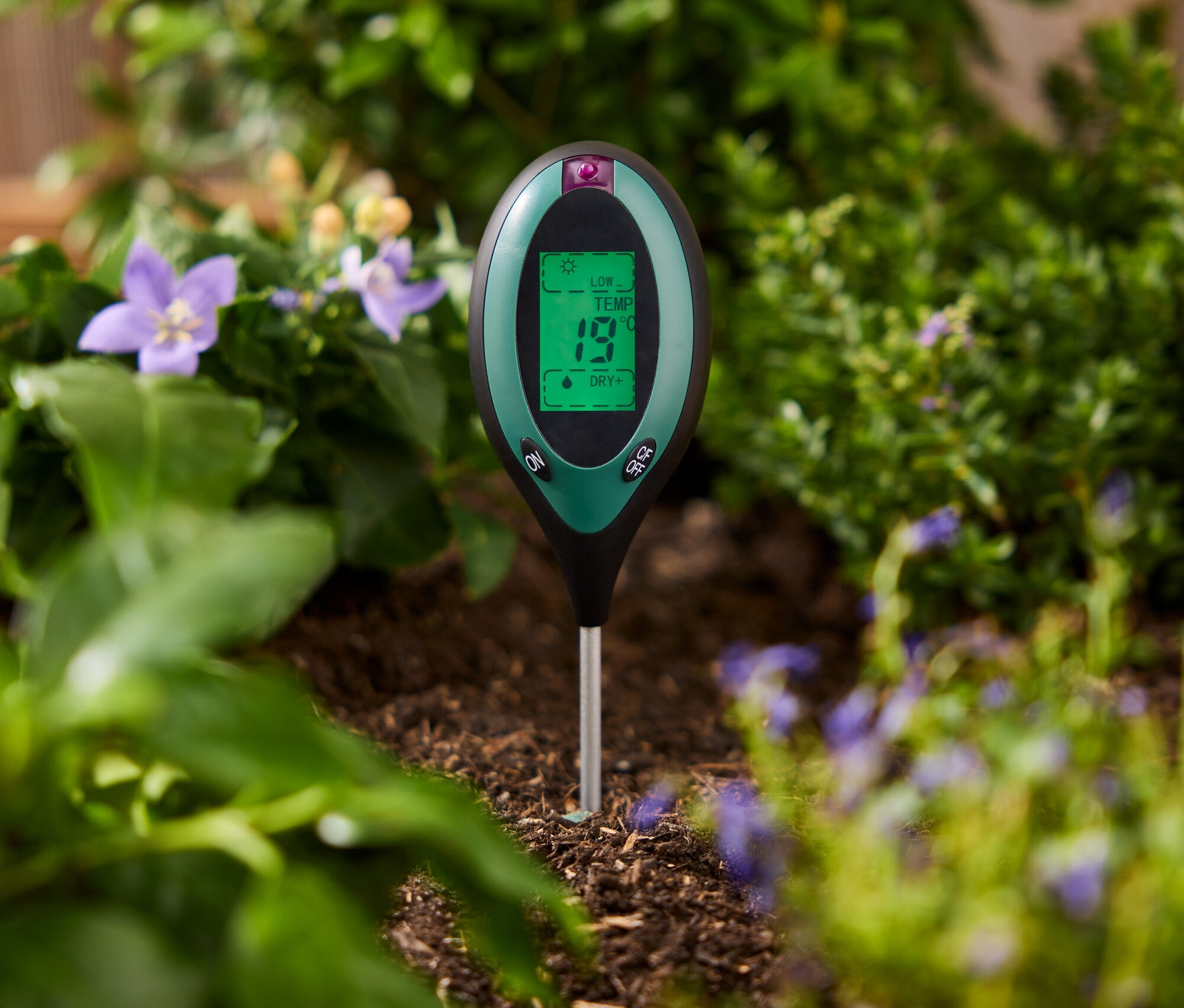 Zelený merač pôdy zapichnutý v zemi medzi rastlinami.