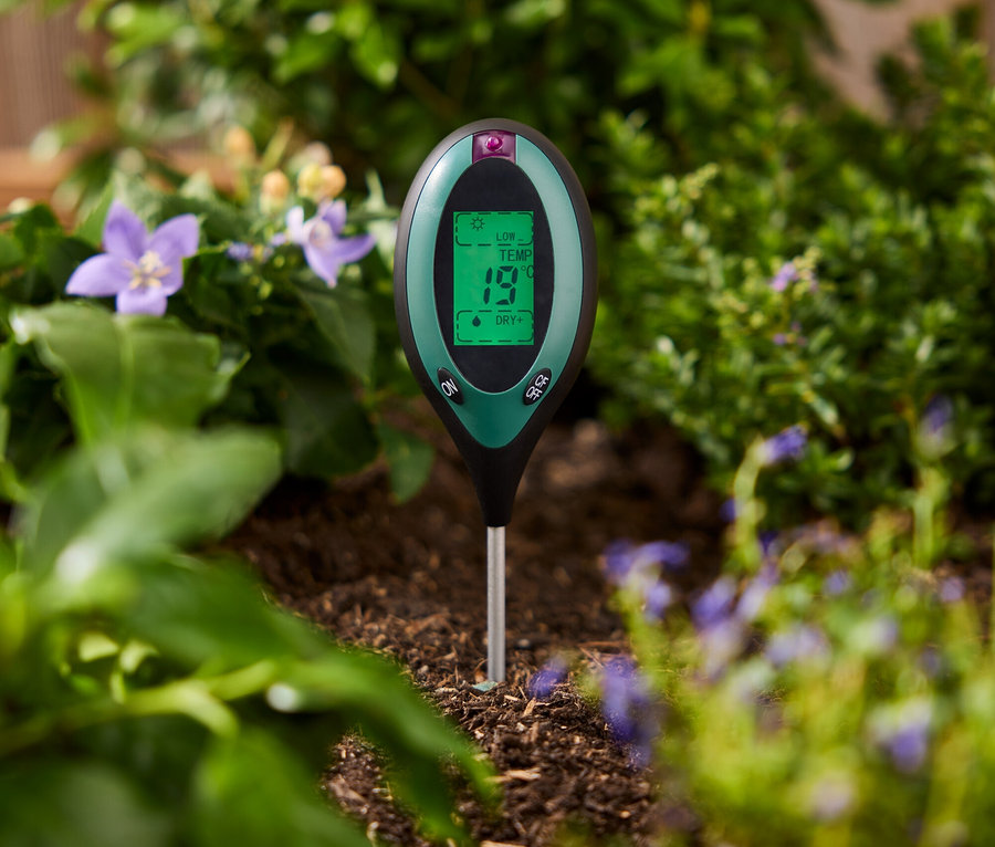 Zelený merač pôdy zapichnutý v zemi medzi rastlinami.