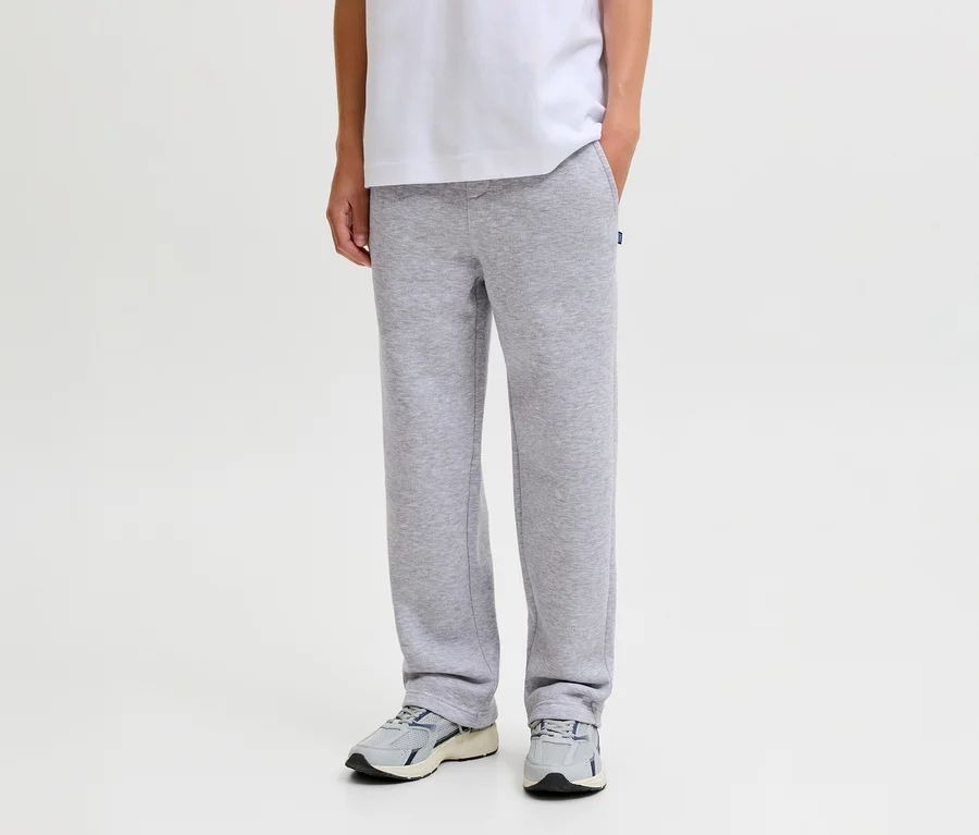 Osoba v sivých teplákoch Jack&Jones Bradley, bielom tričku a sivých teniskách, s jednou rukou vo vrecku.