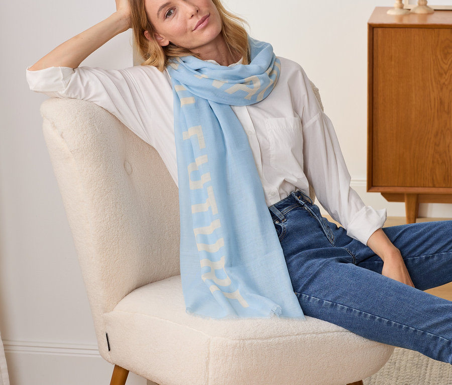 Žena sedí v kresle a má na sebe tkaný šál so statement potlačou.