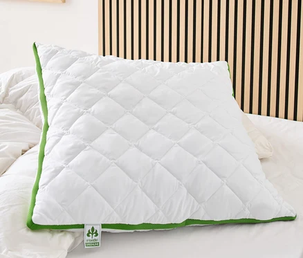 Na posteli leží biely prešívaný vankúš s klimatizačným pásom irisette® greenline so zeleným lemovaním.