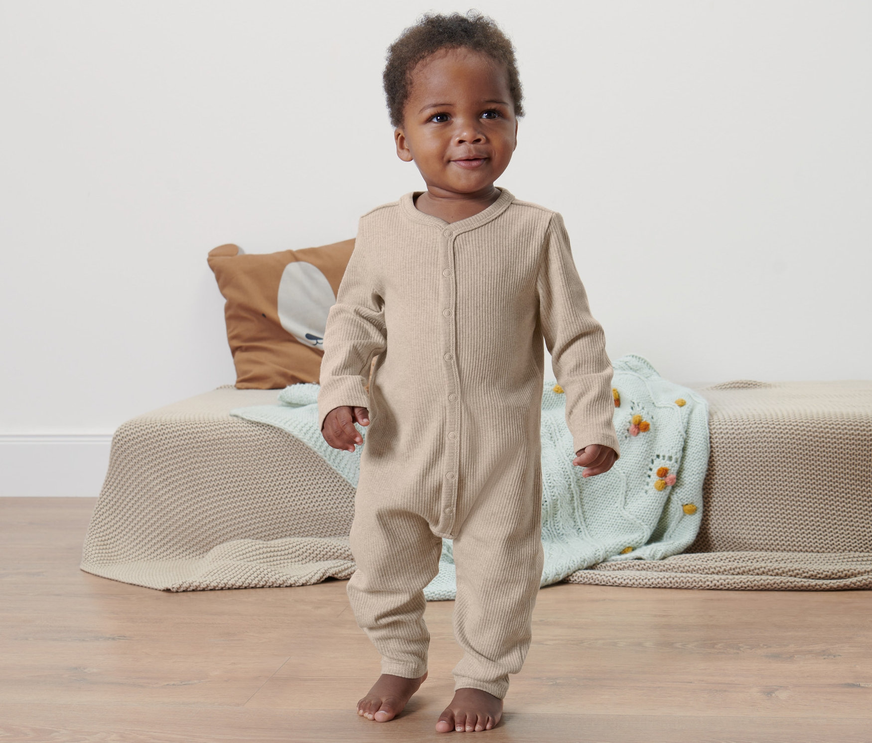 Dieťa tmavej pleti stojí na podlahe a má na sebe detské body.