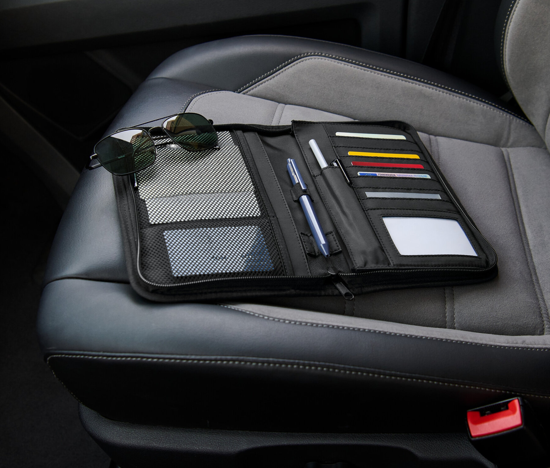 Čierny organizér do priehradky na rukavice leží otvorený na sedadle auta vedľa slnečných okuliarov.