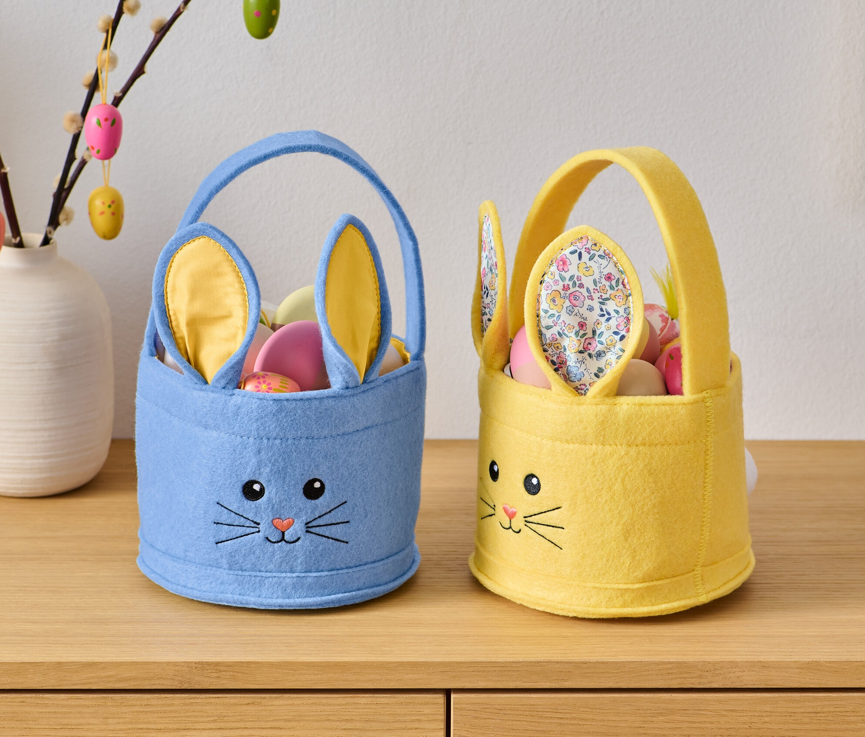Dva veľkonočné košíčky s tvárou králika stoja na drevenej komode.