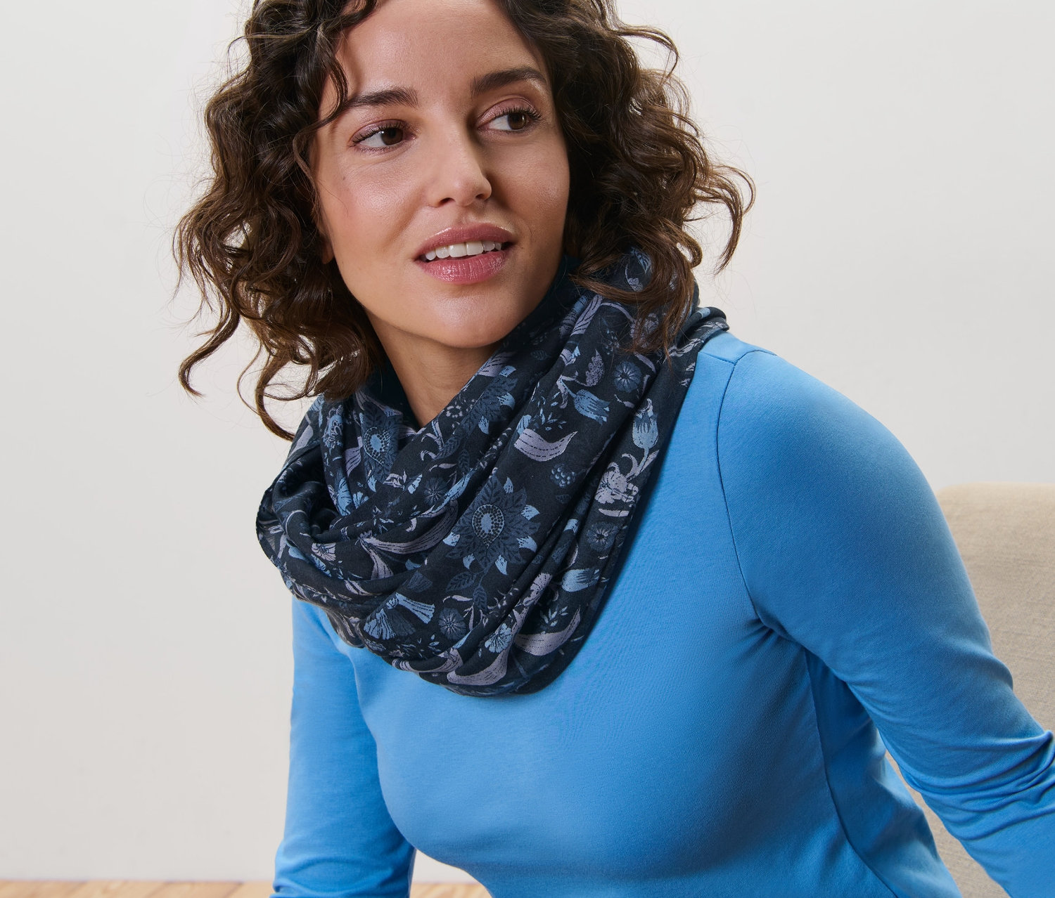 Žena s hnedými vlasmi nosí šál s potlačou.