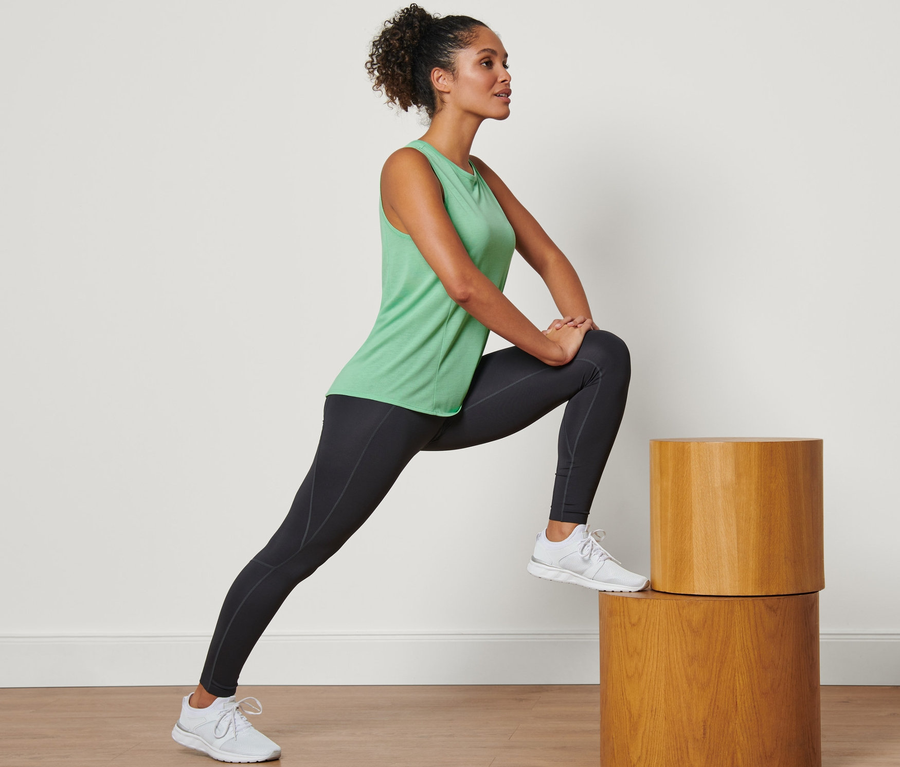 Žena sa pretahuje na drevených stupňoch a má na sebe zelený športový top.