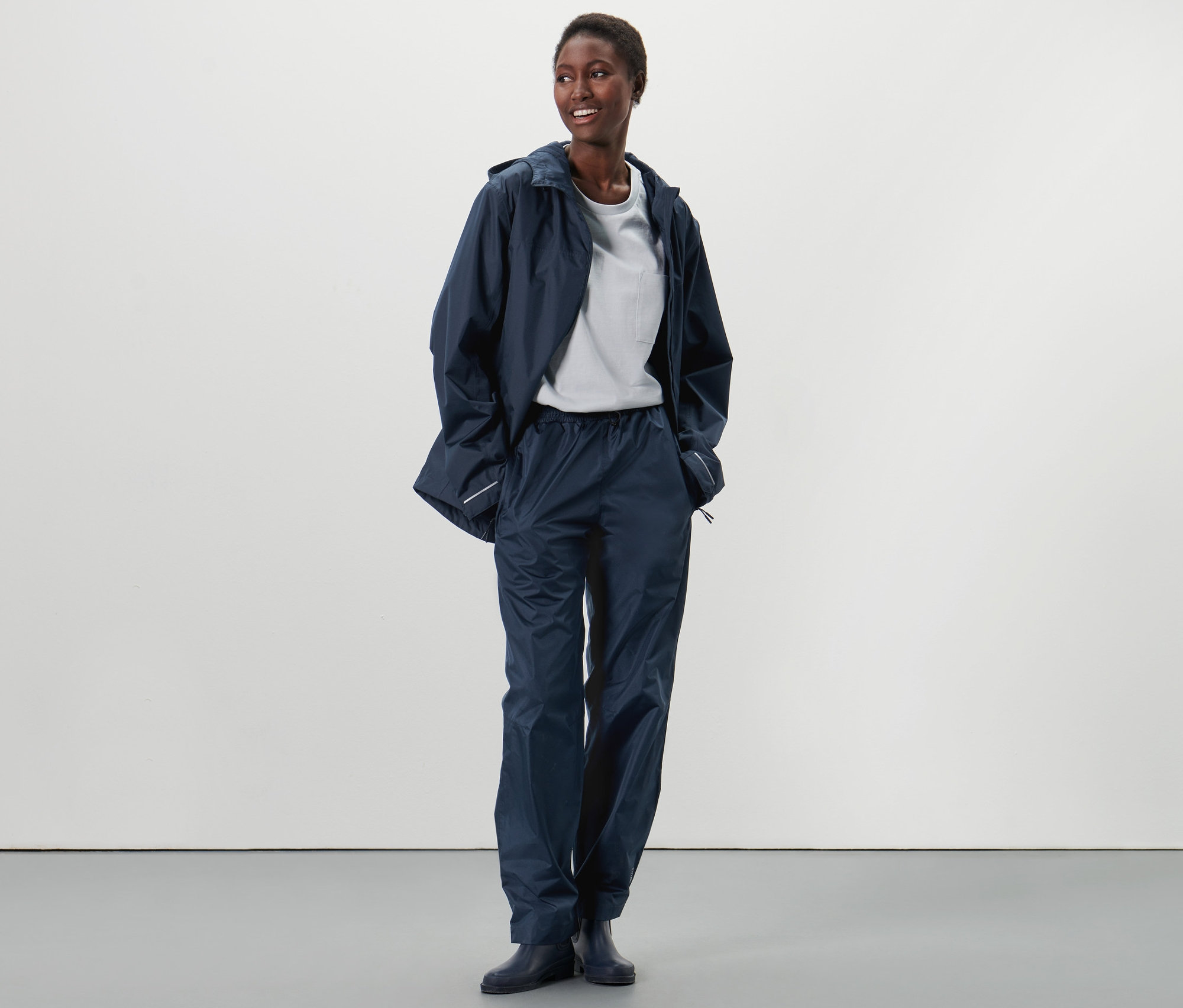 Afroameričanka stojí a má na sebe unisexové nohavice do dažďa a bundu do dažďa.
