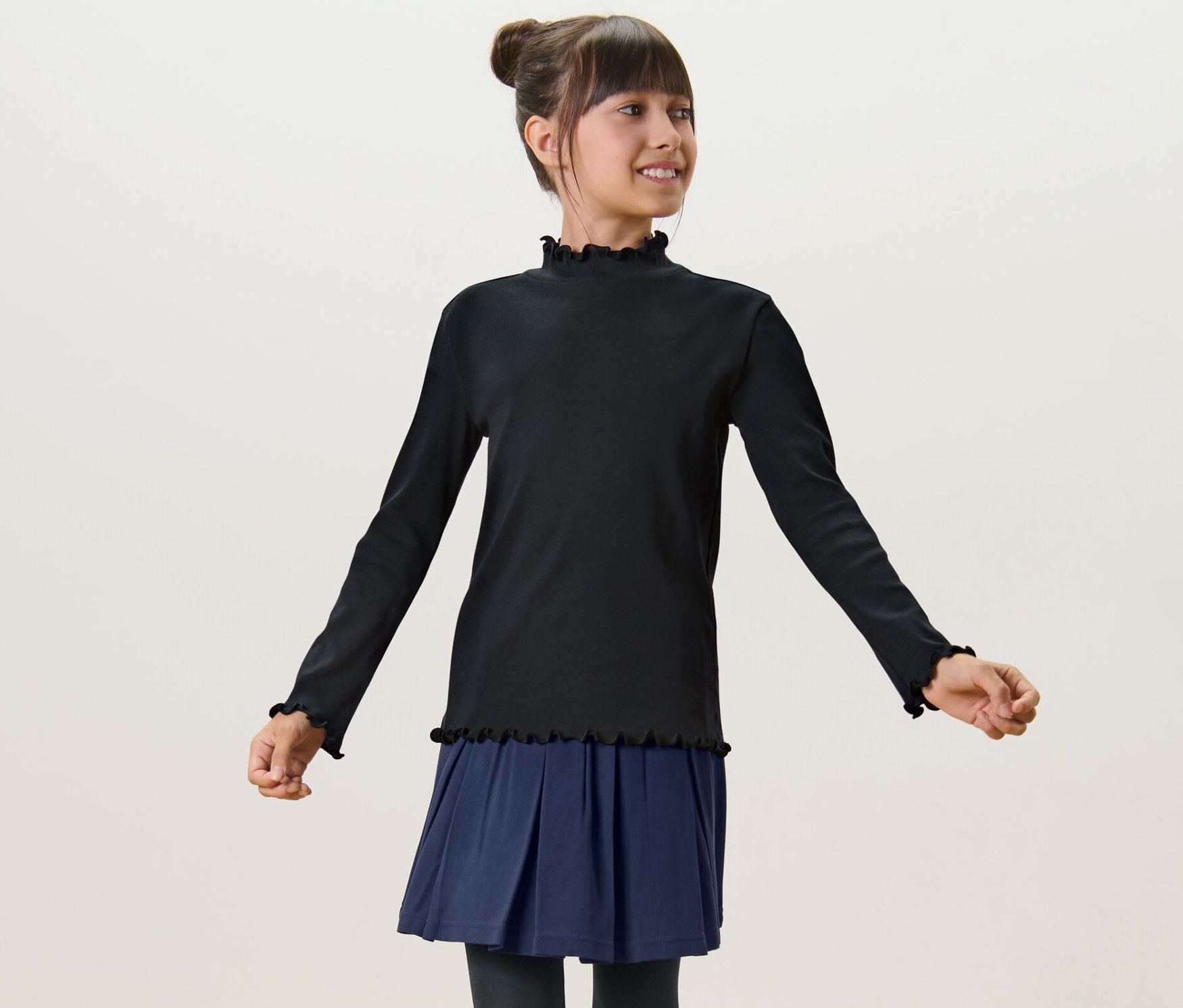 Dievča má na sebe čierne detské tričko s dlhými rukávmi a modrú sukňu.