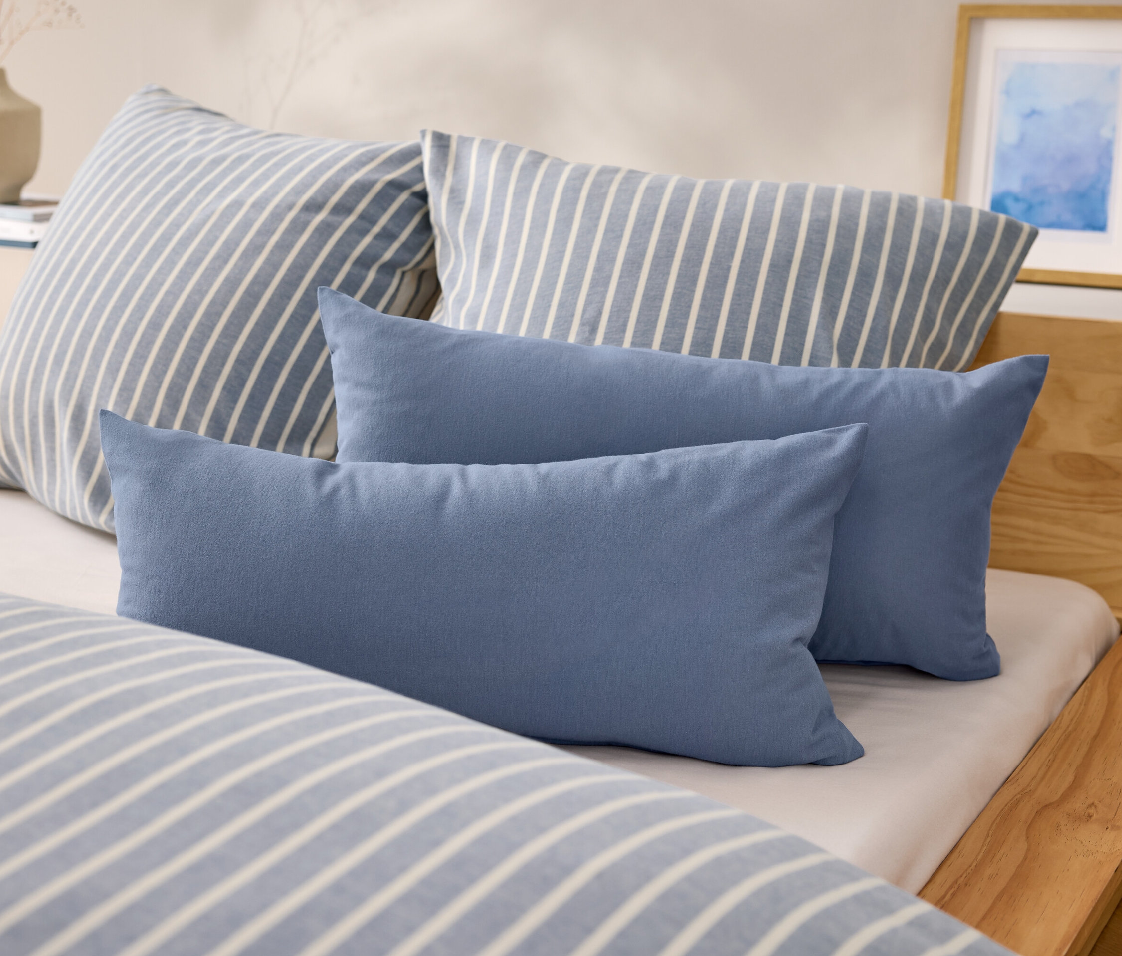 Na posteli sú dva modré obdĺžnikové vankúše a dva vankúše s modrými a bielymi pruhmi.