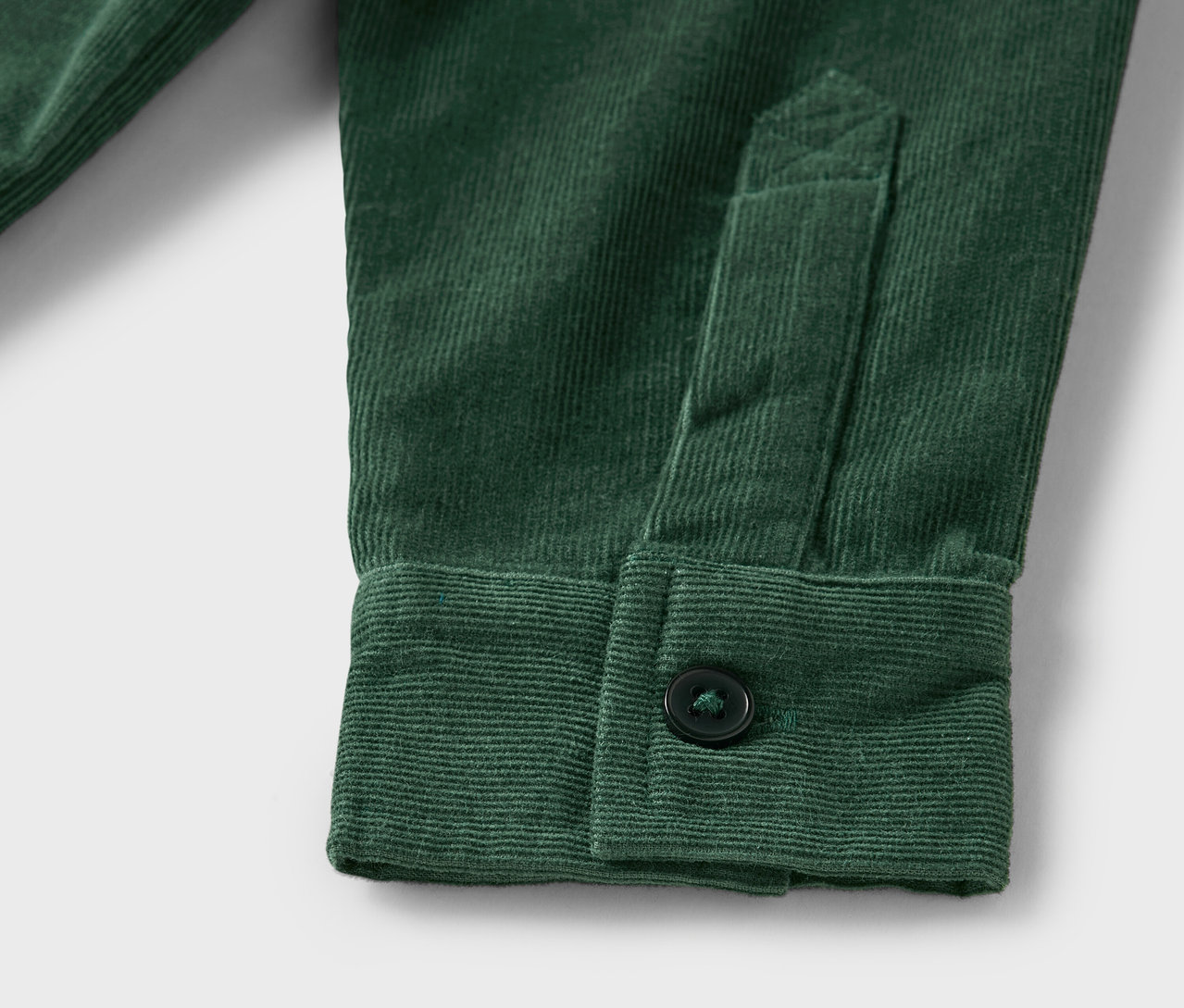 Detail zelené menčestrovej košele s gombíkom na manžete.