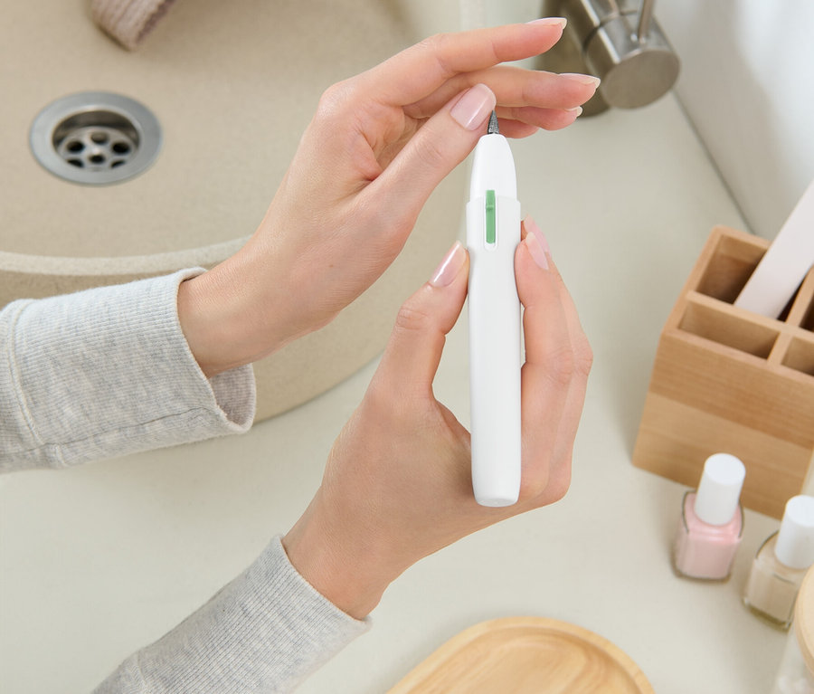 Žena drží bielu frézku na nechty pred umývadlom.