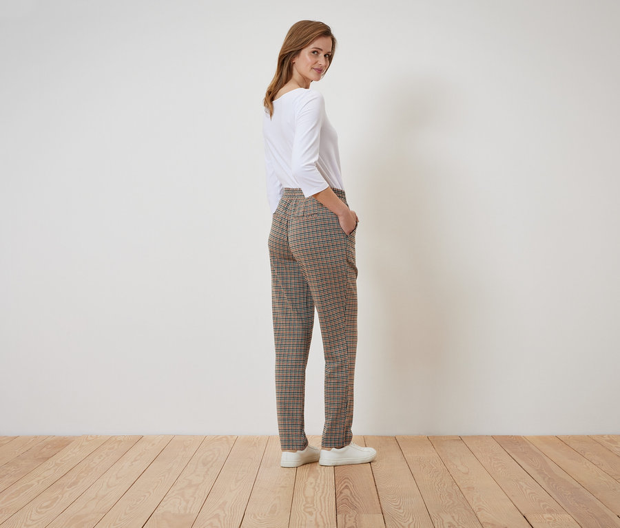 Žena pózuje v kockovaných nohaviciach a bielom tope.