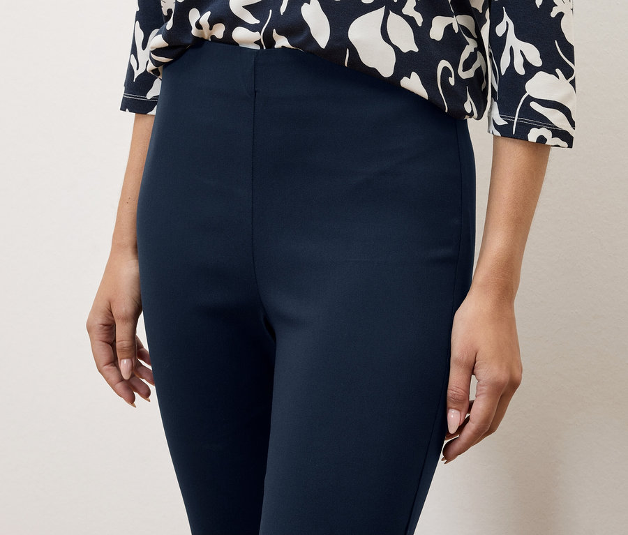 Detailný záber ženy v tmavomodrých nohaviciach a blúzke s kvetinovou potlačou.