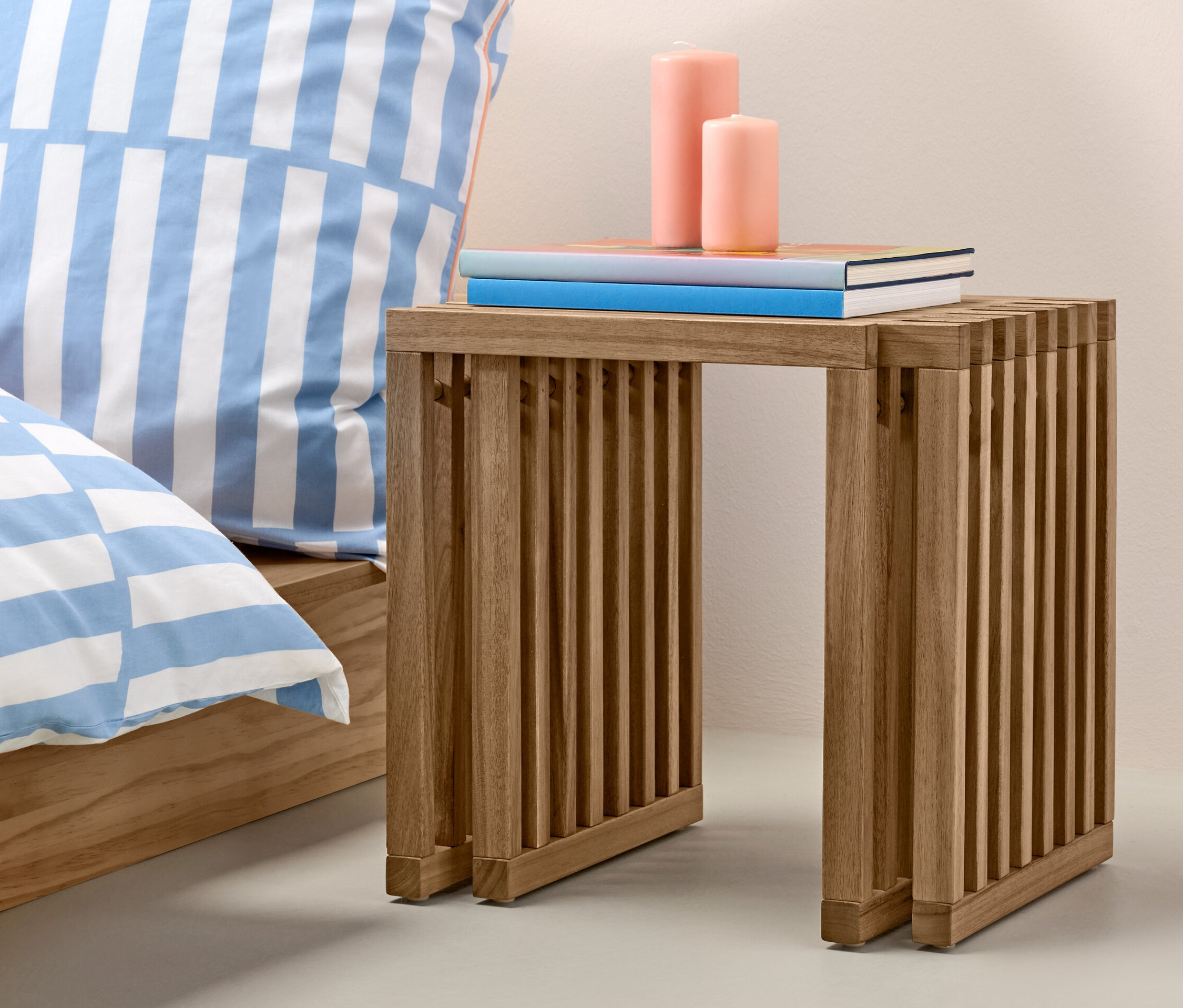 Vysúvací stolček s knihami a sviečkami vedľa postele a oranžovej vázy.