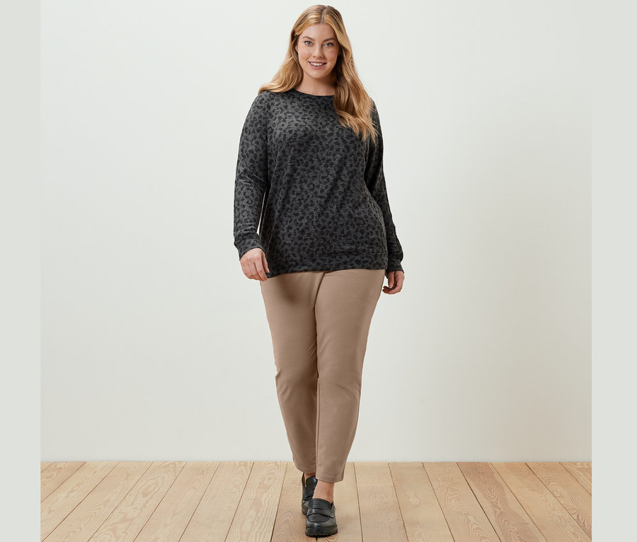 Žena kráča a má na sebe tričko s netopierími rukávmi s potlačou a béžové teplákové nohavice.