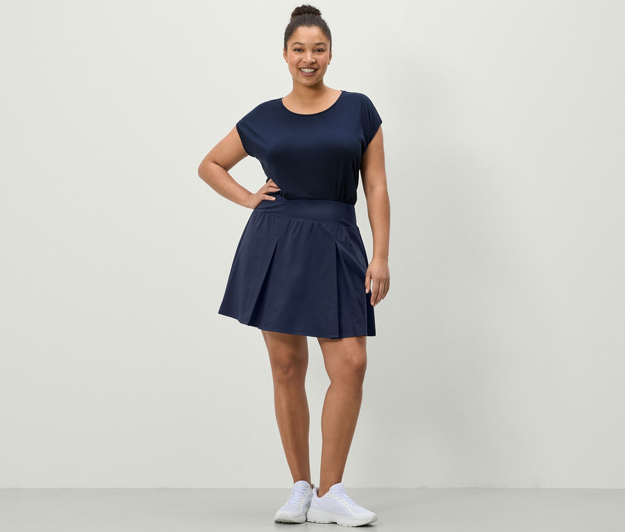 Žena pózuje v športovej sukni tmavomodrej farby a modrom športovom tričku.