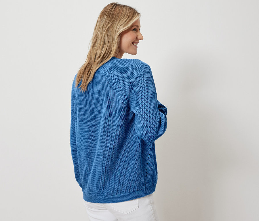 Žena pózuje v otvorenom kardigáne a bielych džínsoch.