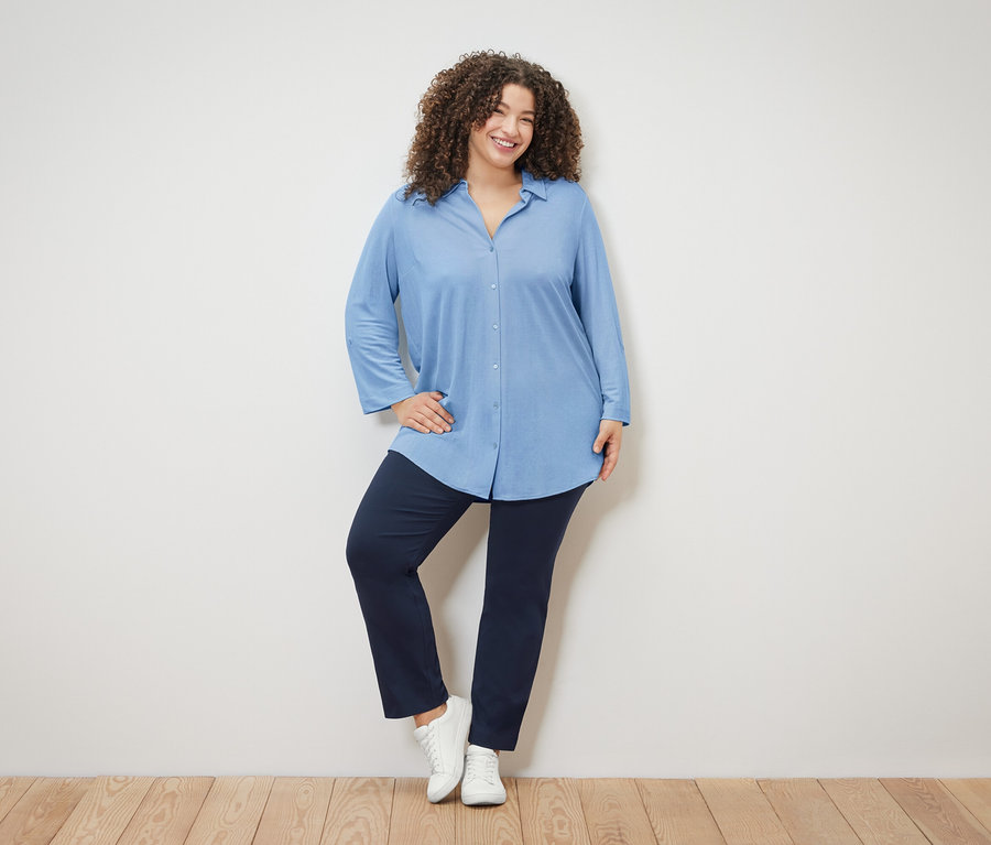 Žena s kučeravými vlasmi má na sebe svetlomodrú blúzku, tmavomodré nohavice a biele topánky.