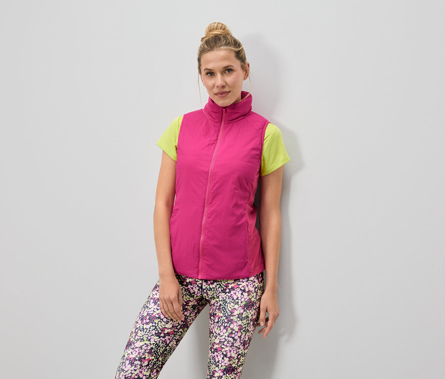 Žena má na sebe ružovú vestu cez svetlozelené tričko a kvetinové legíny.