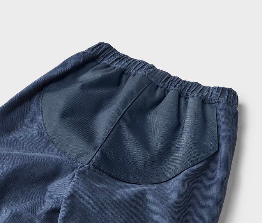 Detail modrých menčestrových nohavíc s elastickým pásom a našitým zadným vreckom.