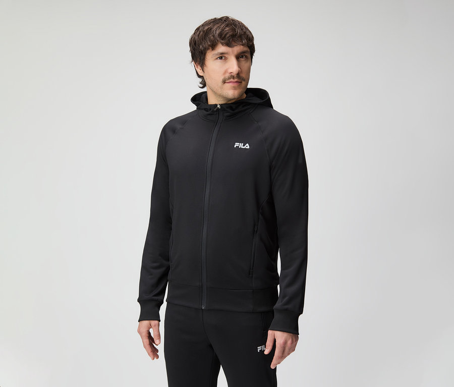 Muž s fúzmi má na sebe čiernu teplákovú súpravu Fila s kapucňou.