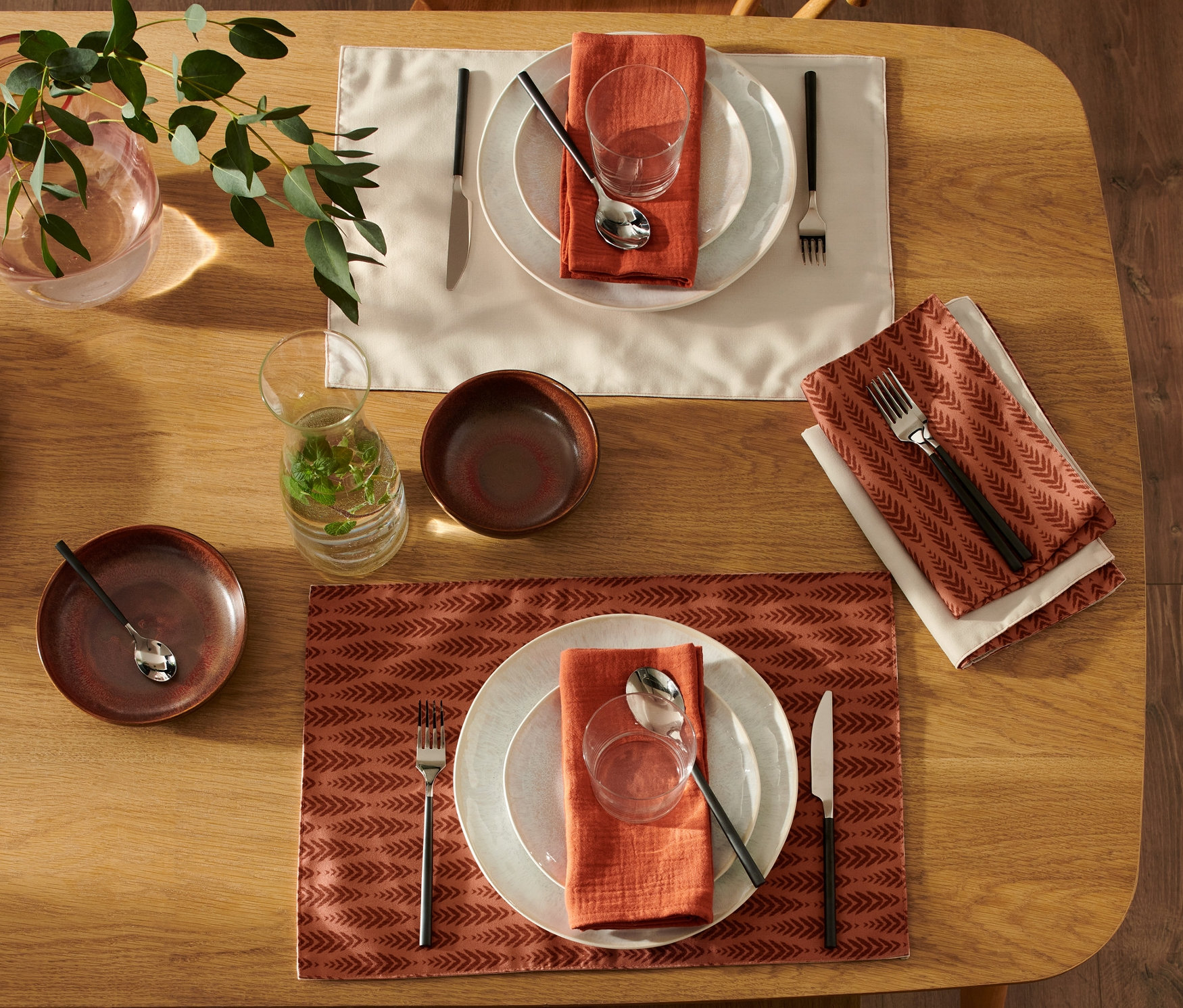 Dva prestreté stoly s obojstrannými prestieraními, 4 ks, s taniermi, pohármi, príbormi a obrúskami. Na stole váza s rastlinami.