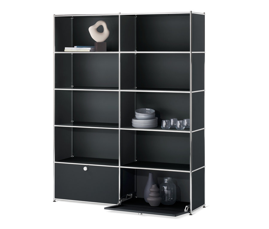 Čierny regál »CN3« s 2 výklopnými dvierkami. Na policiach sú dekorácie, poháre a taniere.