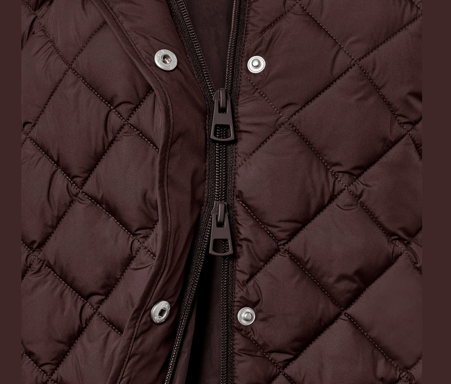 Detailný pohľad na dlhú prešívanú vestu s kapucňou, zapnutú na zips a patentky.