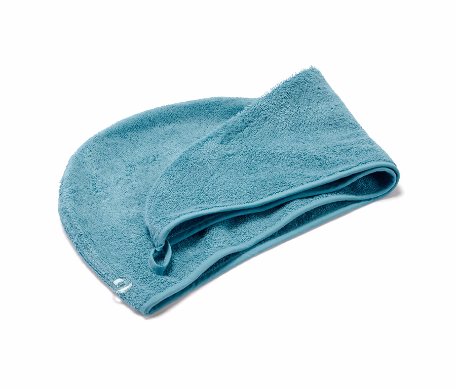 Akvamarínový uterákový turban leží zložený na bielom pozadí.
