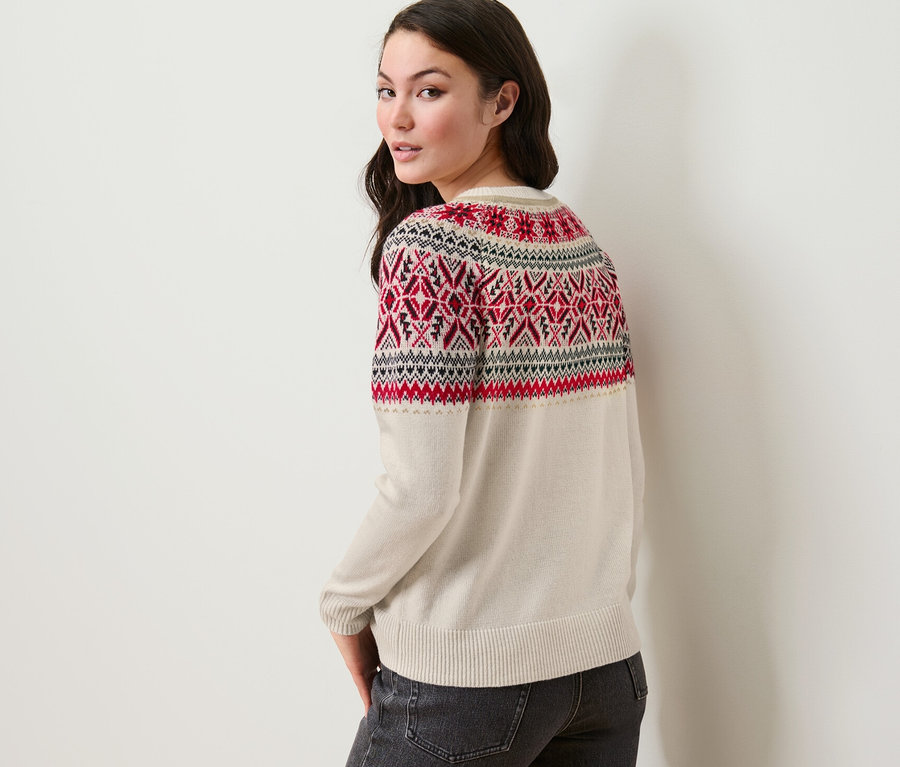 Žena pozerá cez plece a má na sebe pletený pulóver s nórskym vzorom a džínsy.